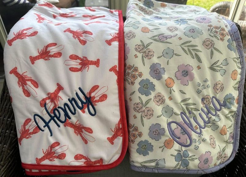 Two baby blankets, one with lobsters and Henry in navy script, one floral with Olivia in lavender script