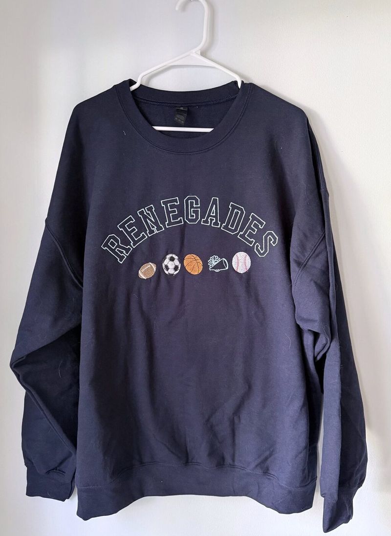 Navy crewneck with RENEGADES arched in white outline letters above a row of embroidered sports balls