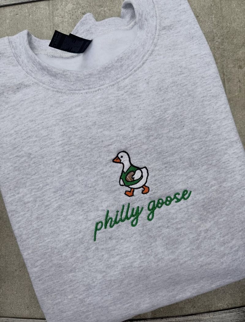 Heather crewneck with an embroidered goose holding a football above philly goose in green script